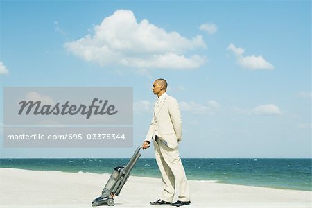 Man in suit standing on beach, using vacuum cleaner, side view