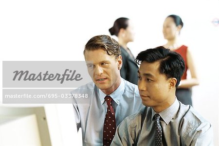 Two businessmen looking at desktop computer together, women standing in background