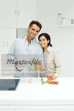 Couple cooking together in kitchen, both smiling at camera