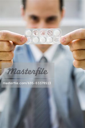 Businessman holding up package of tablets, looking at camera, focus on foreground