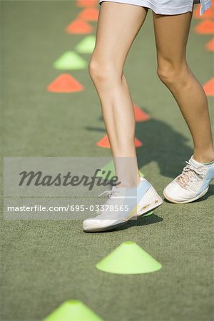 Teenage girl running through plastic cones, low angle view, cropped