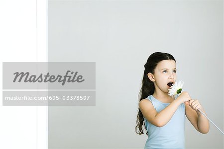Little girl singing into flower, looking away