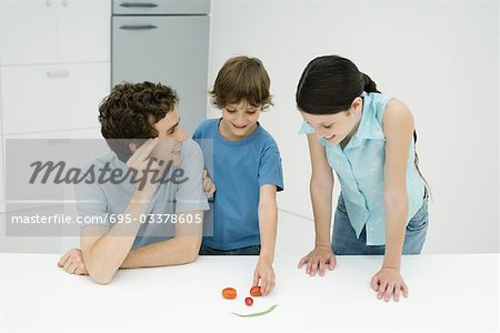 Father and two children in kitchen, making smiley face out of vegetables