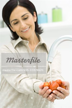 Woman rising handful of tomatoes under faucet, smiling