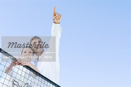 Man standing outdoors with daughter, pointing at the sky, both looking up and smiling, low angle view