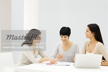 Trois femmes assis à table, discutant des document, souriant
