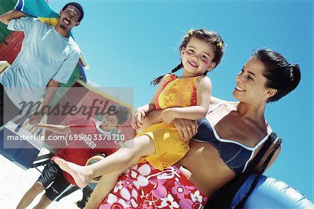 Family walking at the beach, mother carrying daughter, girl smiling at camera