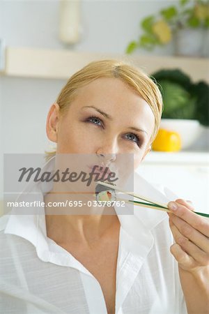 Woman holding up maki sushi with chopsticks, looking up, puckering lips