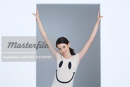 Preteen girl wearing smiley face tee-shirt, arms raised, smiling at camera