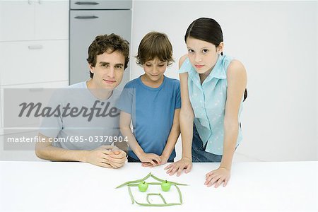 Man with boy and girl in kitchen, with house made out of food