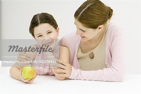 Woman and girl, girl holding apple, smiling at camera