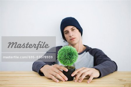Jeune homme assis à table, tenant des bonsaïs, regardant la caméra
