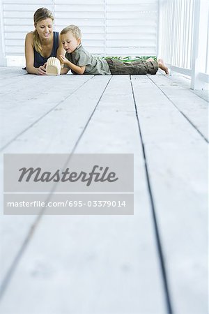 Mother and son lying on deck, looking at wooden object, low angle view