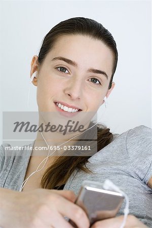 Teenage girl listening to MP3 player, smiling at camera