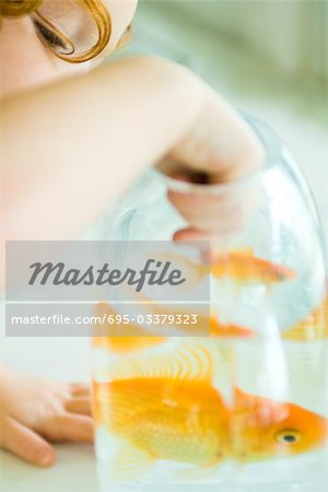 Girl reaching into goldfish bowl, cropped