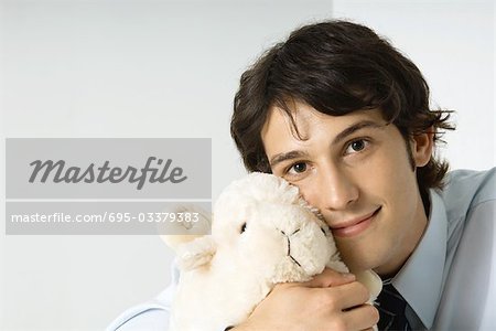 Jeune homme jouet en peluche tenant contre joue, souriant à la caméra