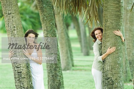 Mère et fille teen étreindre les troncs d'arbres, souriant à la caméra