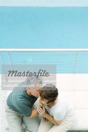 Couple sitting on balcony, man kissing woman's cheek, high angle view