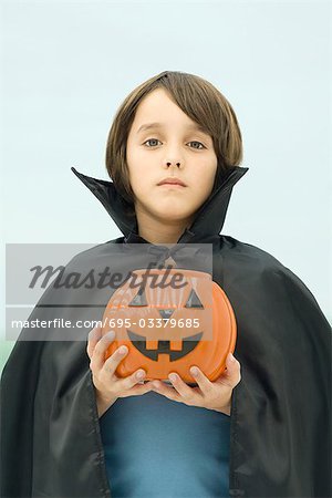 Boy dressed in vampire costume, holding jack o' lantern, portrait