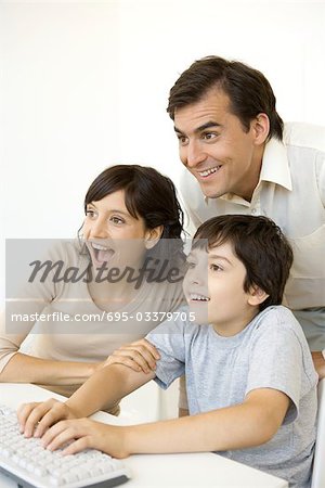Little boy playing computer video game while his parents watch, all smiling