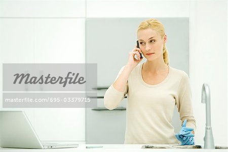 Junge Frau in der Küche stehen, halten Gummihandschuhe, Handy verwenden