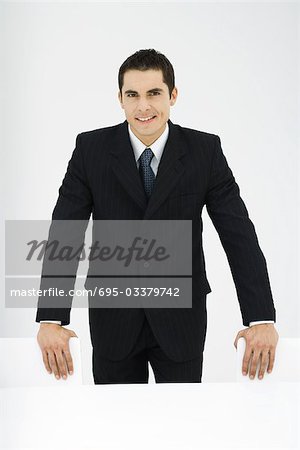 Businessman smiling at camera, standing, hands on chairs, portrait