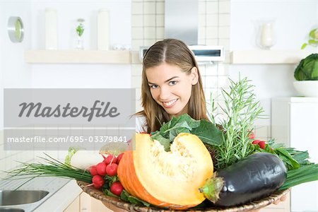 Woman holding tray of fresh vegetables, smiling at camera