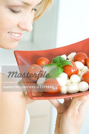 Woman holding up tomato mozzarella salad, smiling, cropped view