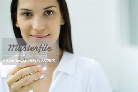 Woman holding glass of water, smiling at camera