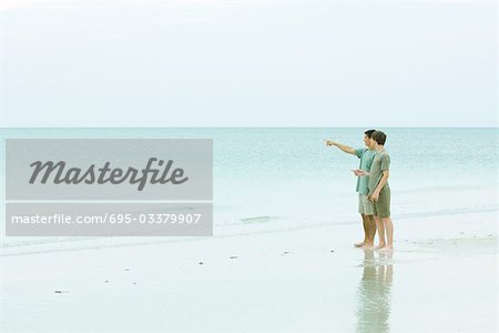 Man and teen boy standing at the beach, looking at view, man pointing