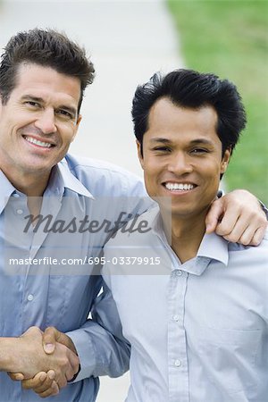 Two businessmen shaking hands, both smiling at camera, high angle view