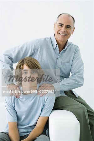 Père et fils assis sur le canapé, les mains de l'homme sur les épaules du jeune garçon, portrait