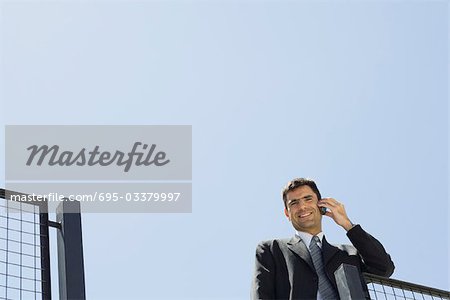 Businessman using cell phone outdoors, smiling at camera, low angle view