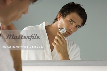 Man looking at himself in mirror, shaving, wearing bathrobe