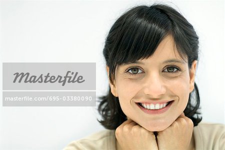 Woman smiling at camera, hands under chin, portrait