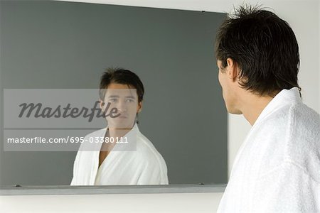 Mann im Bademantel selbst im Spiegel betrachten