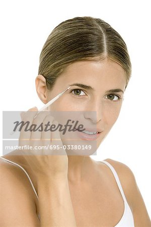 Woman applying eye make-up with brush, looking at camera