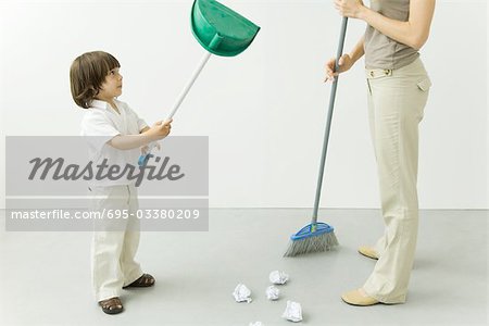 Petit garçon jouant avec pan de poussière tandis que sa mère est de balayer le sol, recadrée vue