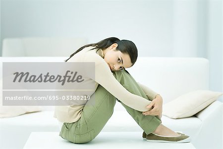 Frau sitzt am Kaffeetisch, umarmt Knien, Blick in die Kamera