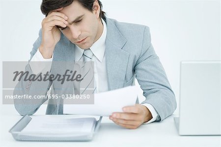 Young businessman sitting at desk, holding head and looking down at document