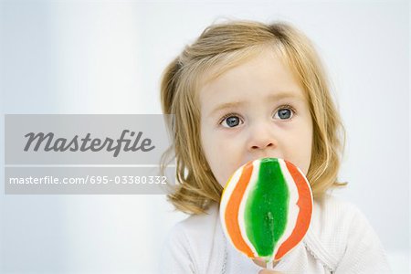 Little girl eating large lollipop, looking up