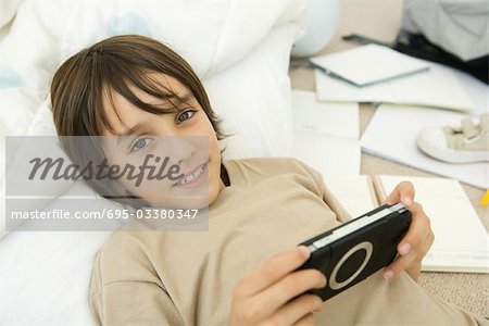 Garçon tenant portable de jeu vidéo, couchée et souriant à la caméra