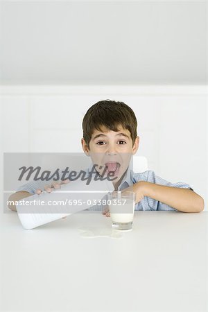 Boy pouring milk into glass, mouth open, spilled milk on table