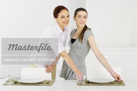 Mère et fille teen affectant la table ensemble, souriant à la caméra