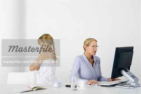 Femme assise à table à l'aide de bureau, fille debout à proximité avec son dos tourné et bras plié