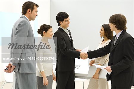 Business associates meeting, shaking hands while others watch