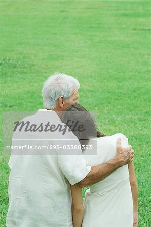 Grandfather with teenage granddaughter, arm around her shoulder, her head on his shoulder