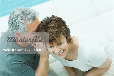 Woman looks away smiling as her husband whispers in her ear