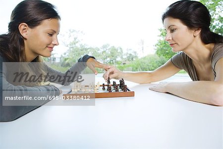 Two women playing chess, one making a move, the other touching her hand