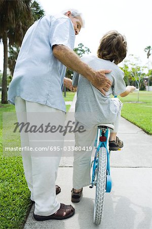 Senior man helping his grandson learn to ride a bicycle